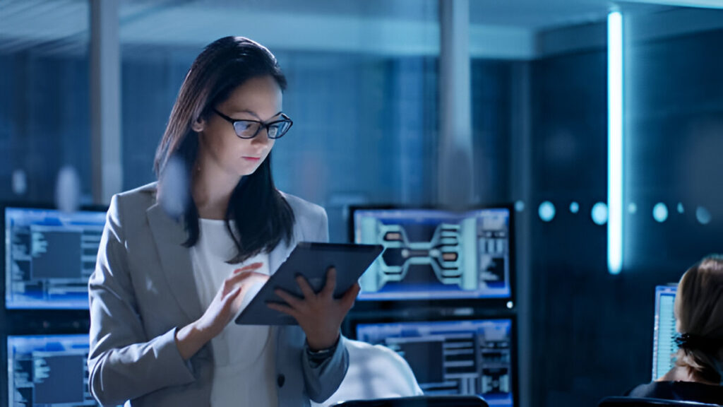 Cybersecurity professional in a blazer using a tablet in a modern control room with digital displays.